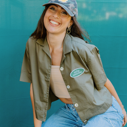 “Upcycled women’s button-up shirt with ‘Aloha Everyday’ vintage patch worn in a beachy, casual setting, showcasing relaxed island style.”